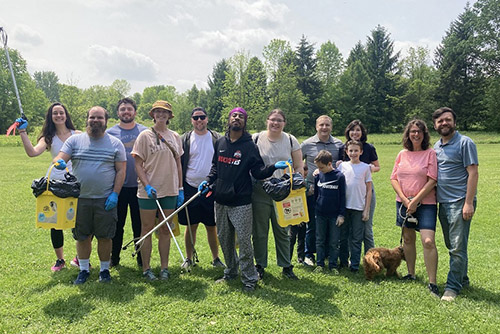 A group of happy coworkers hold trash pickers and buckets to collect garbage in a park
